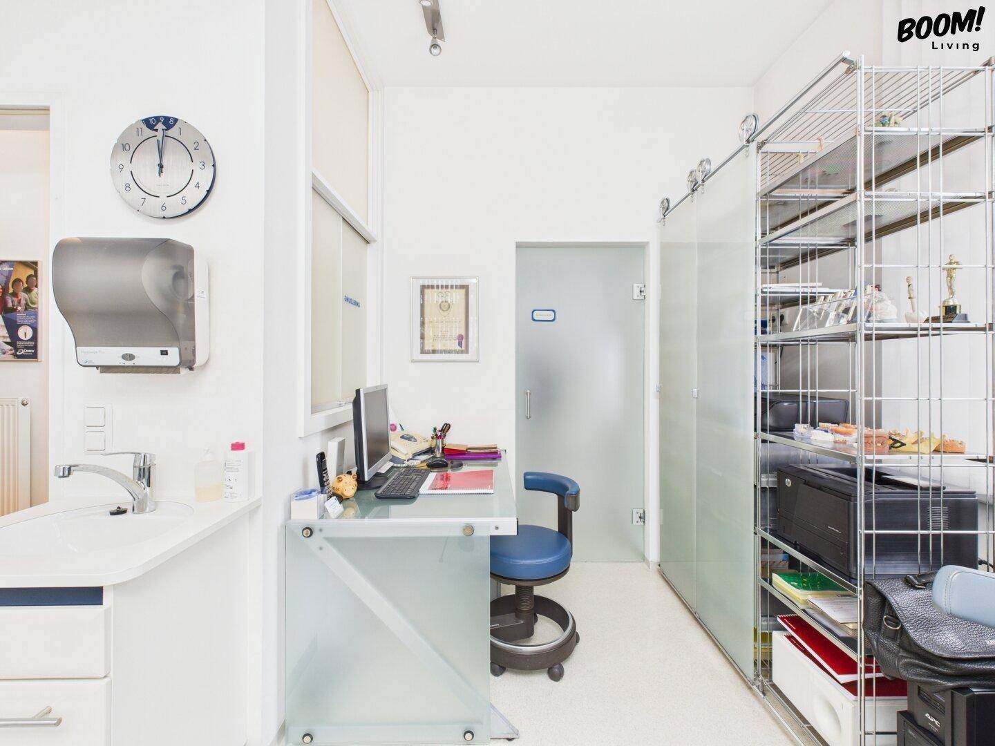 Funktionaler Bürobereich mit Schreibtisch, Waschbecken und offenen Metallregalen für Stauraum.
