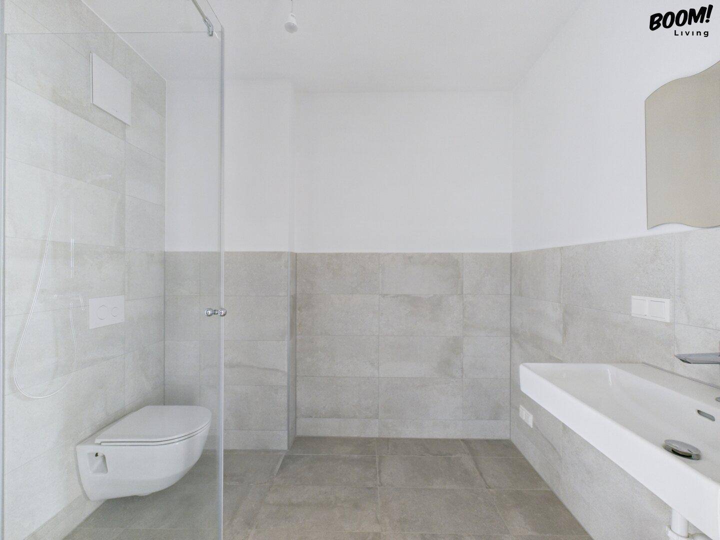 Modernes, leeres Badezimmer mit begehbarer Dusche, Wand-WC und hellen Fliesen.
