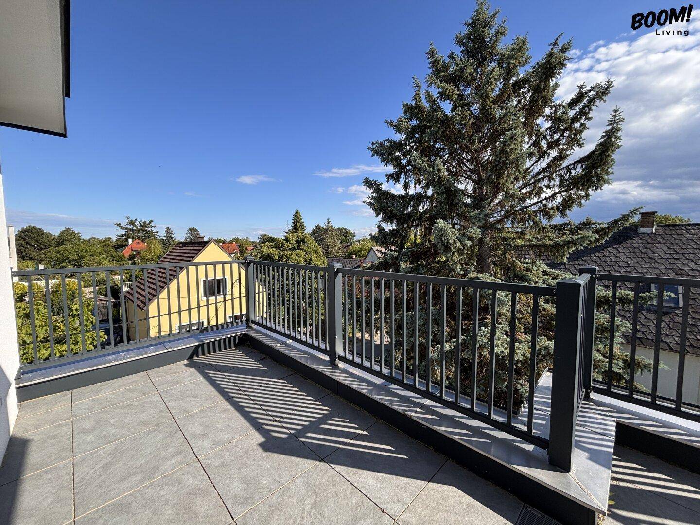 Geräumiger Balkon mit Fliesenboden und Metallgeländer, umgeben von Bäumen.