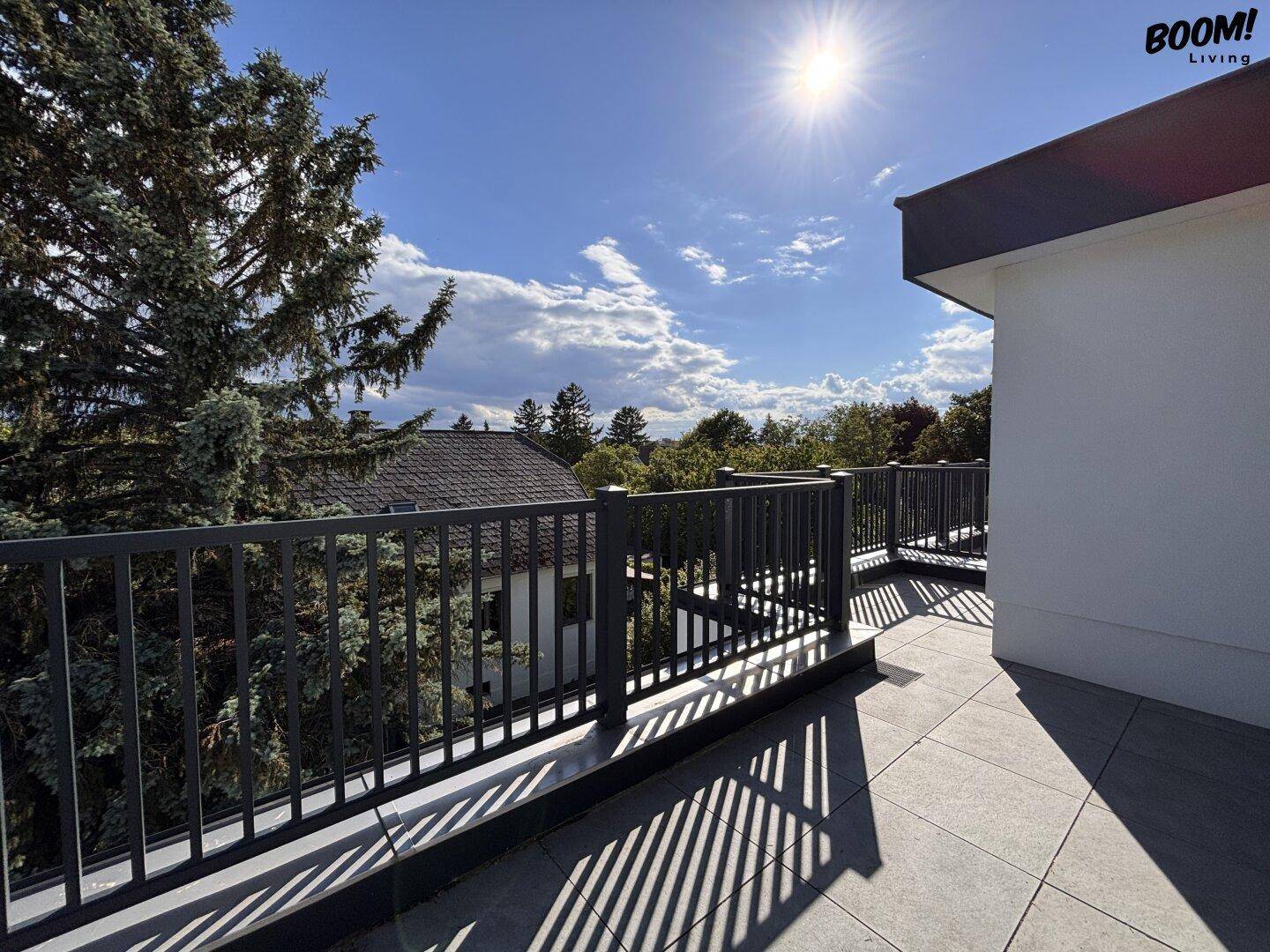 Sonniger Balkon mit Fliesenboden und weitem Blick über die Dächer und Bäume.