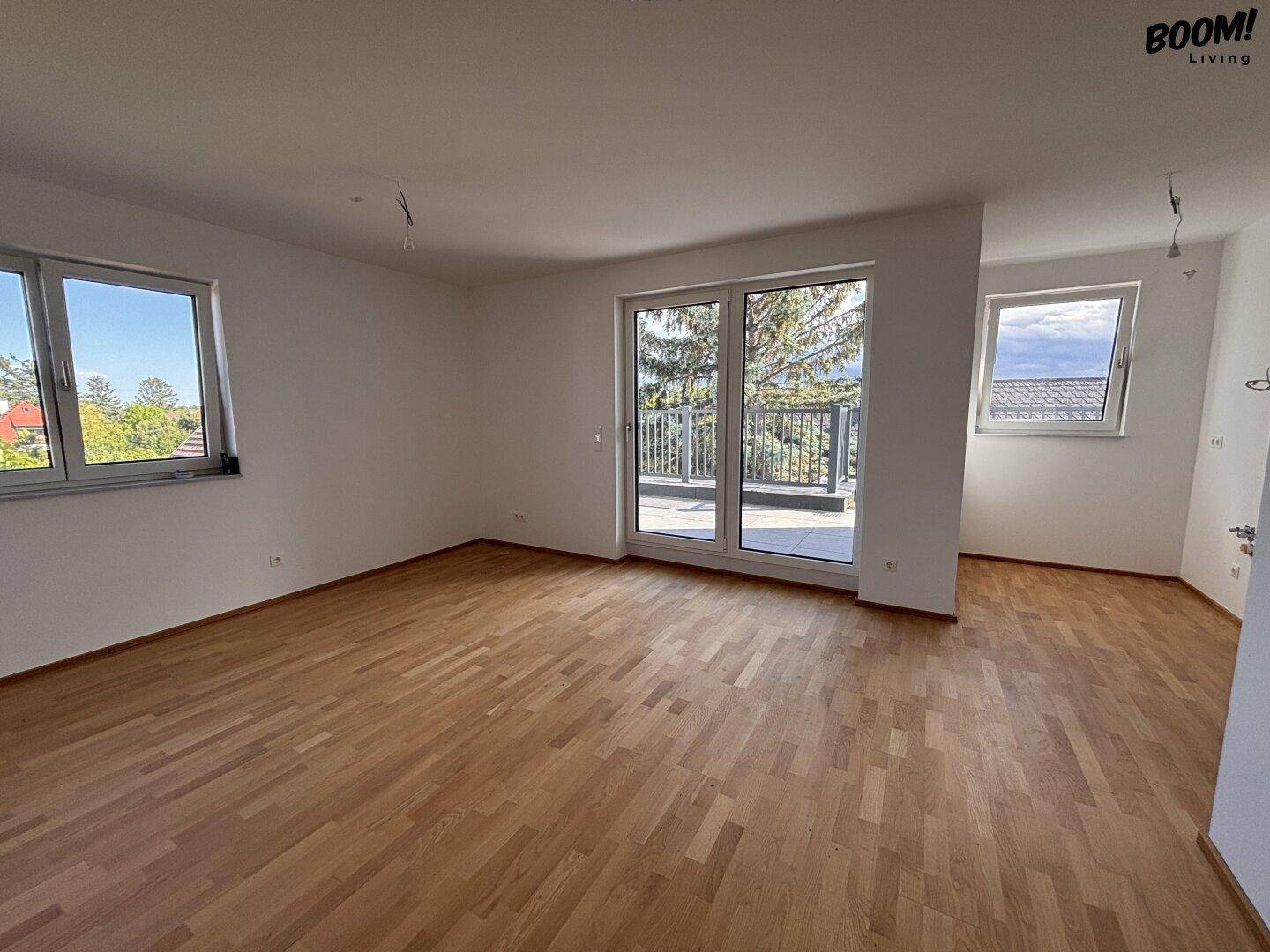 Geräumiger, unmöblierter Wohn-Essbereich mit Holzboden und Zugang zum Balkon.
