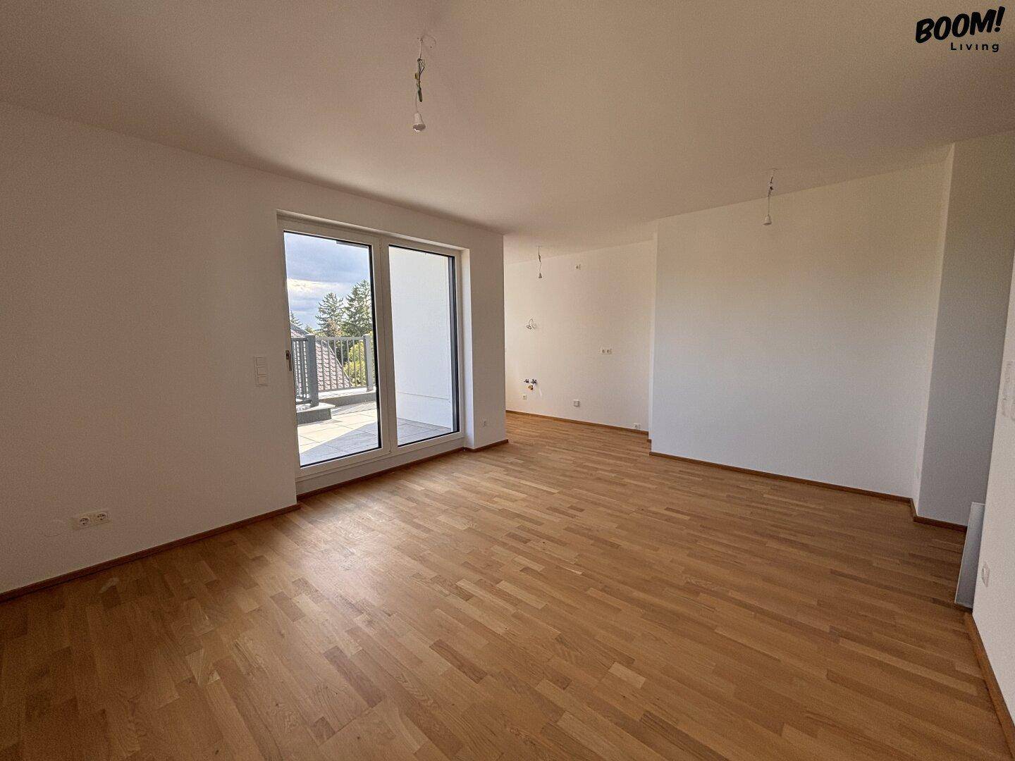 Heller, unmöblierter Wohnbereich mit Holzboden und großen Fenstern.
