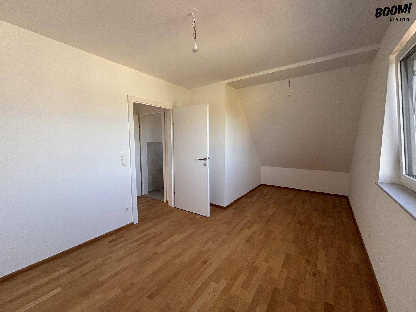 Unmöbliertes Schlafzimmer mit Holzboden, Dachschräge und Fenster.