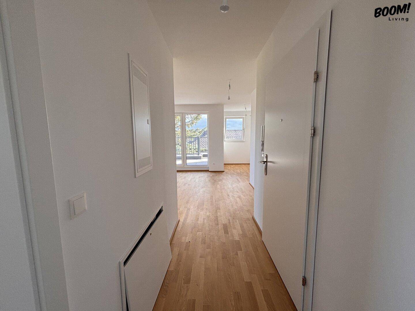 Heller Flur mit Holzboden, weißen Wänden und Blick in den Wohnbereich.