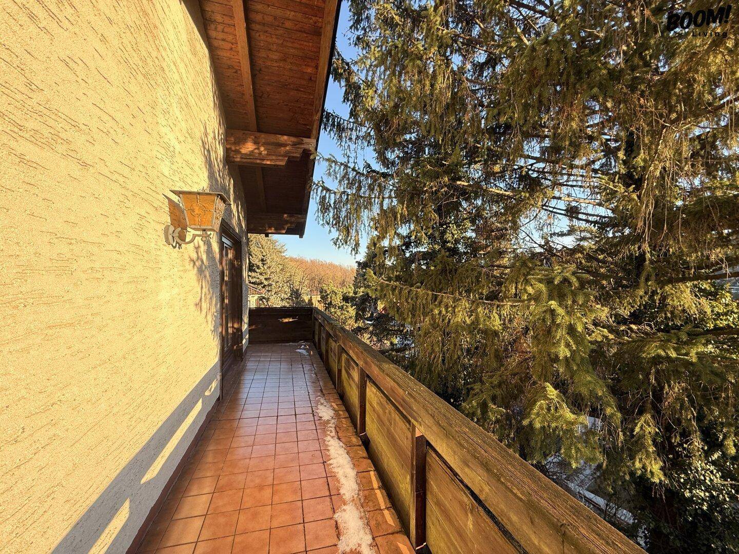 Langer Balkon mit Fliesenboden, Holzgeländer und Blick ins Grüne.