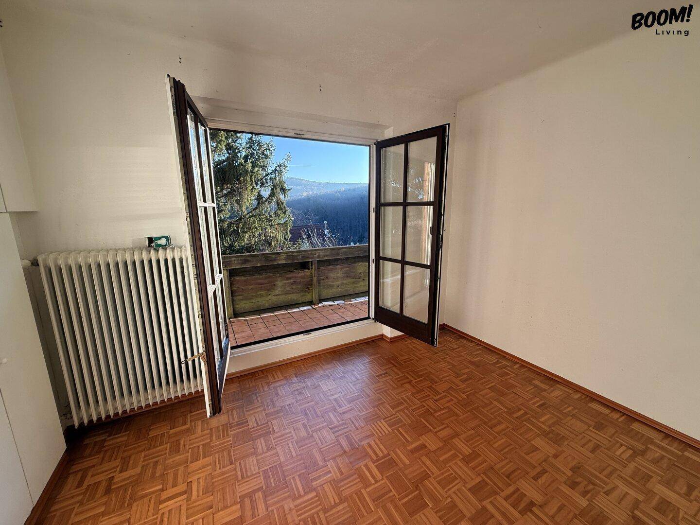 Schlafzimmer mit Parkettboden, Heizkörper und direktem Zugang zu einem Balkon.