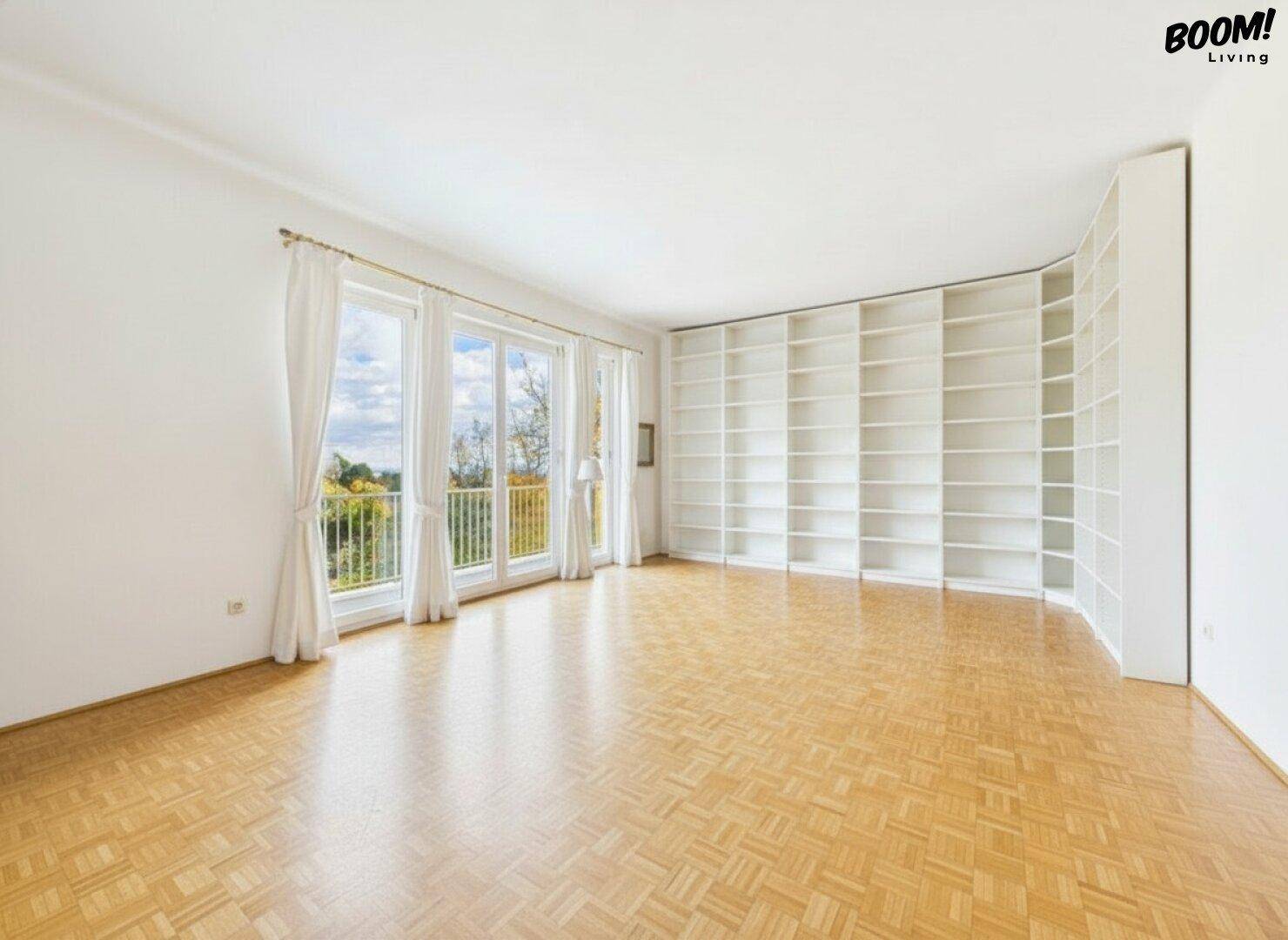 Helles, leeres Wohnzimmer mit Fischgrätparkett, großen Fenstern und einer integrierten Bücherwand.