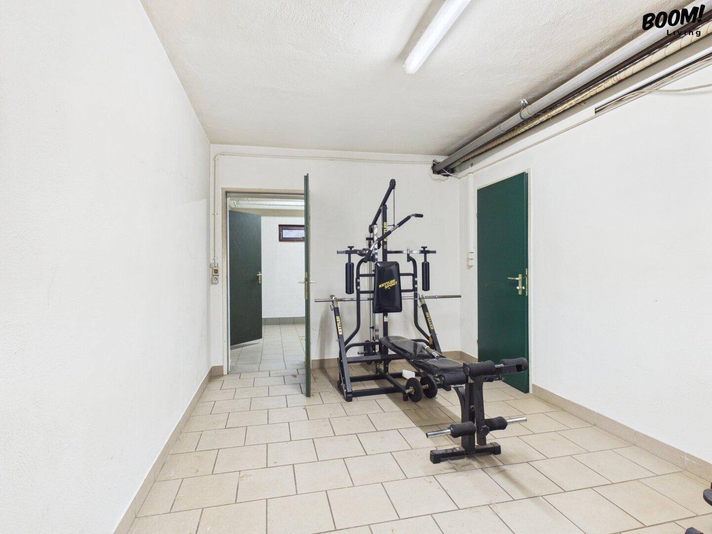 Fitnessraum mit Trainingsgeräten und Fliesenboden, ideal für das tägliche Workout.