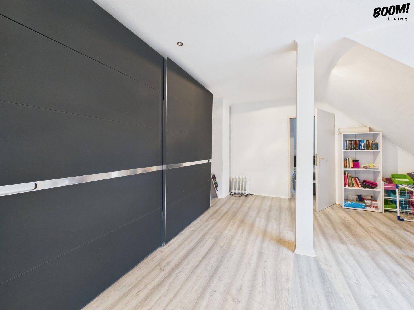 Raum im Dachgeschoss mit Einbauschränken, hellem Laminatboden und schrägen Wänden.