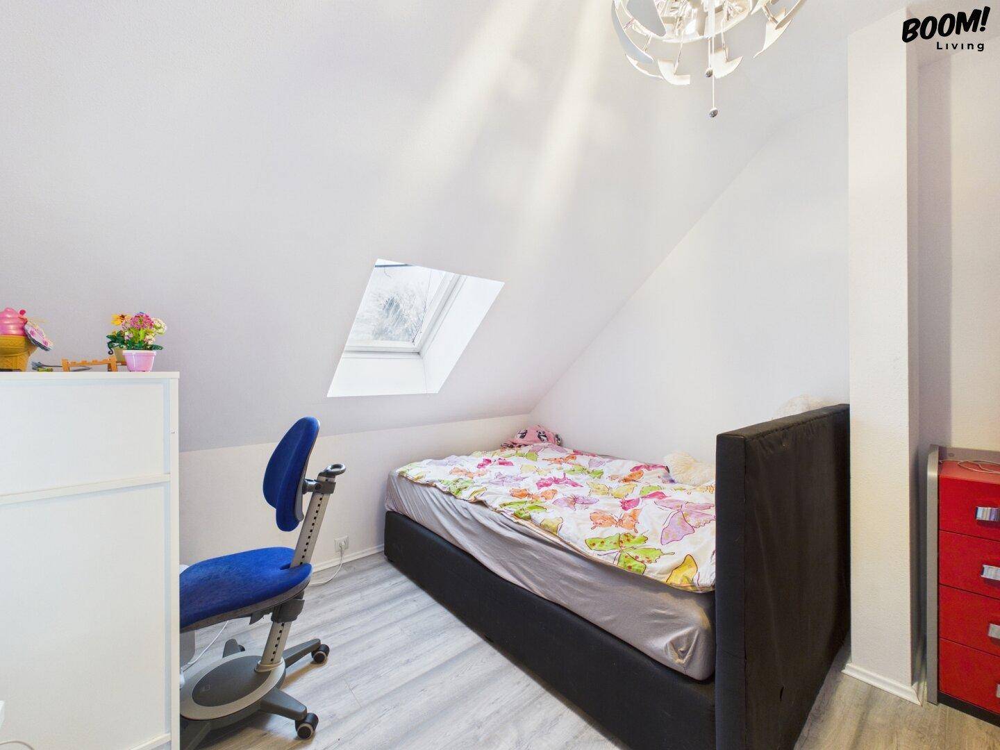 Helles Kinderzimmer im Dachgeschoss mit Dachfenster, Bett und Schreibtisch.