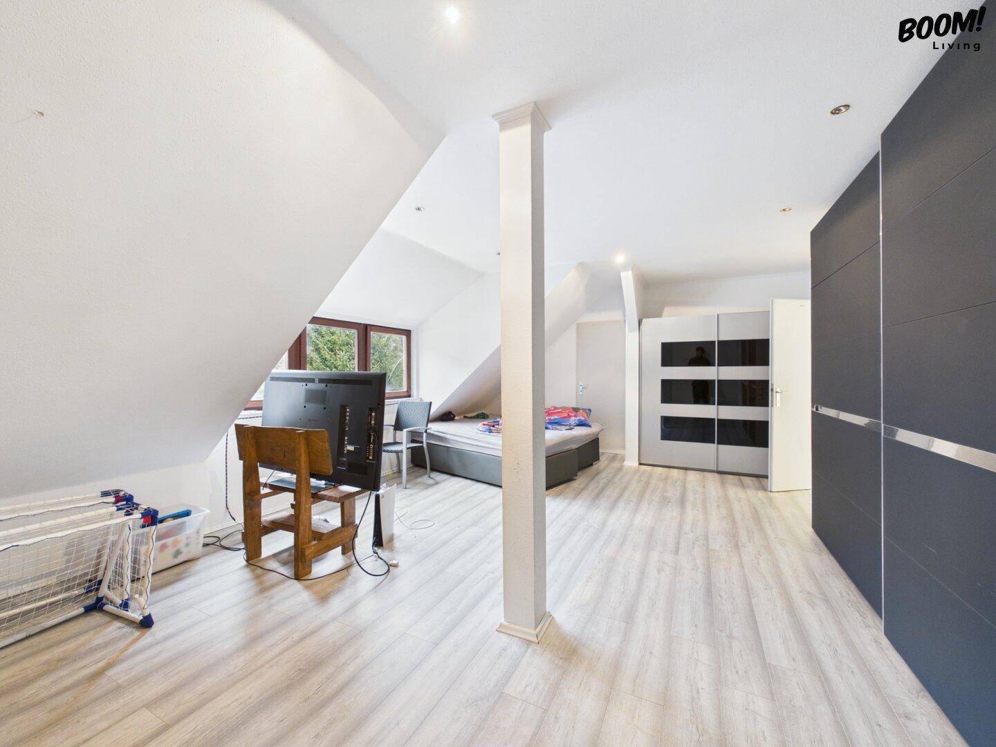 Schlafzimmer im Dachgeschoss mit schrägen Wänden, Einbauschränken und hellem Laminatboden.