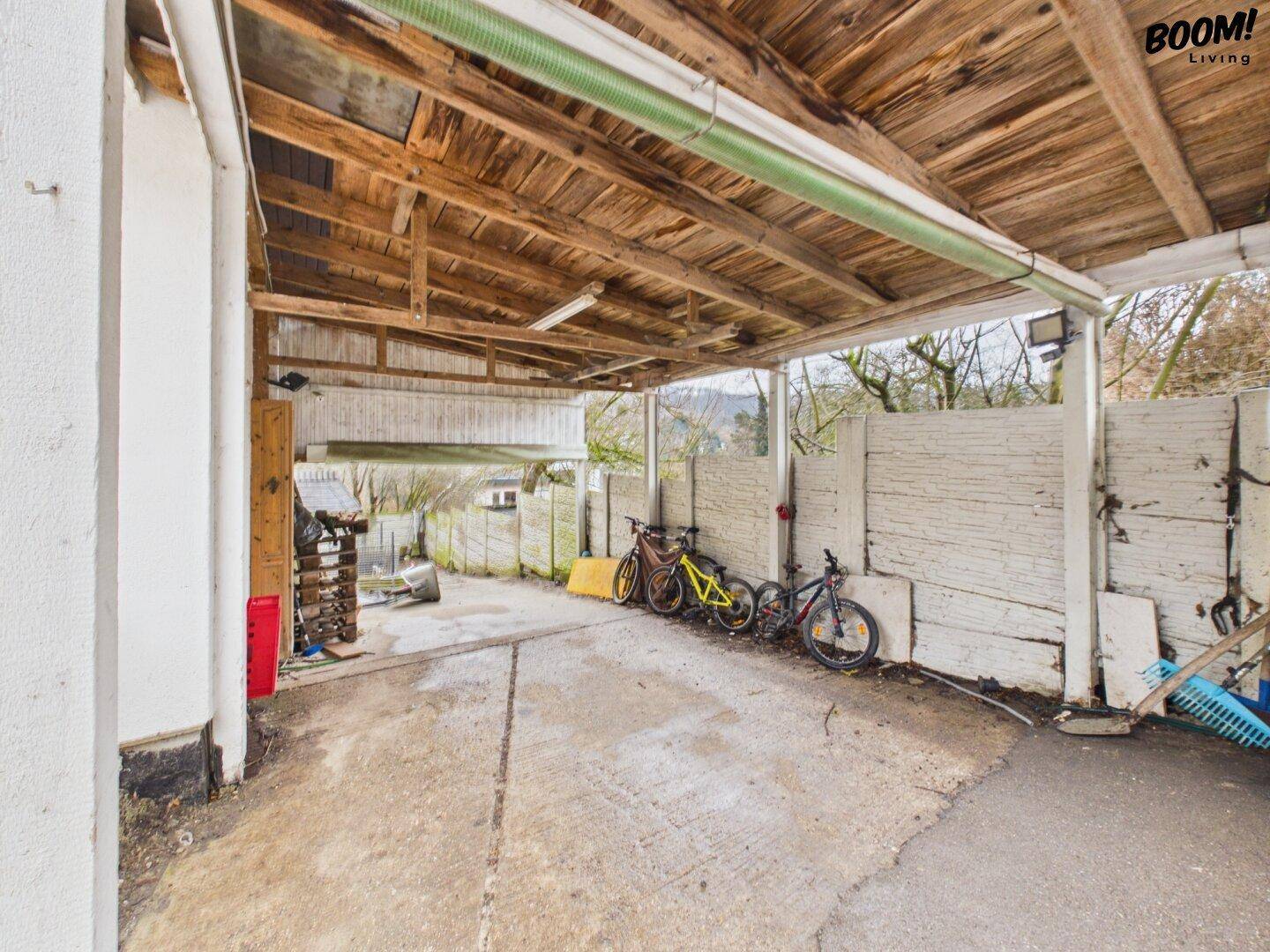 Carport mit Holzkonstruktion, bietet geschützten Stellplatz und Abstellmöglichkeiten für Fahrräder.