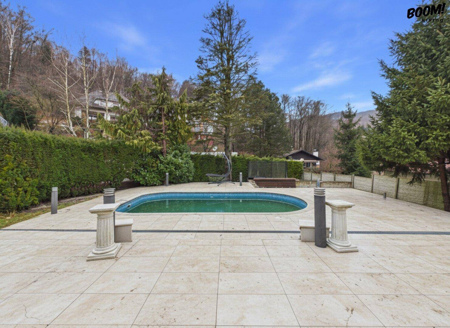 Große gepflasterte Terrasse mit kleinem Pool, umgeben von viel Grün und Bäumen.