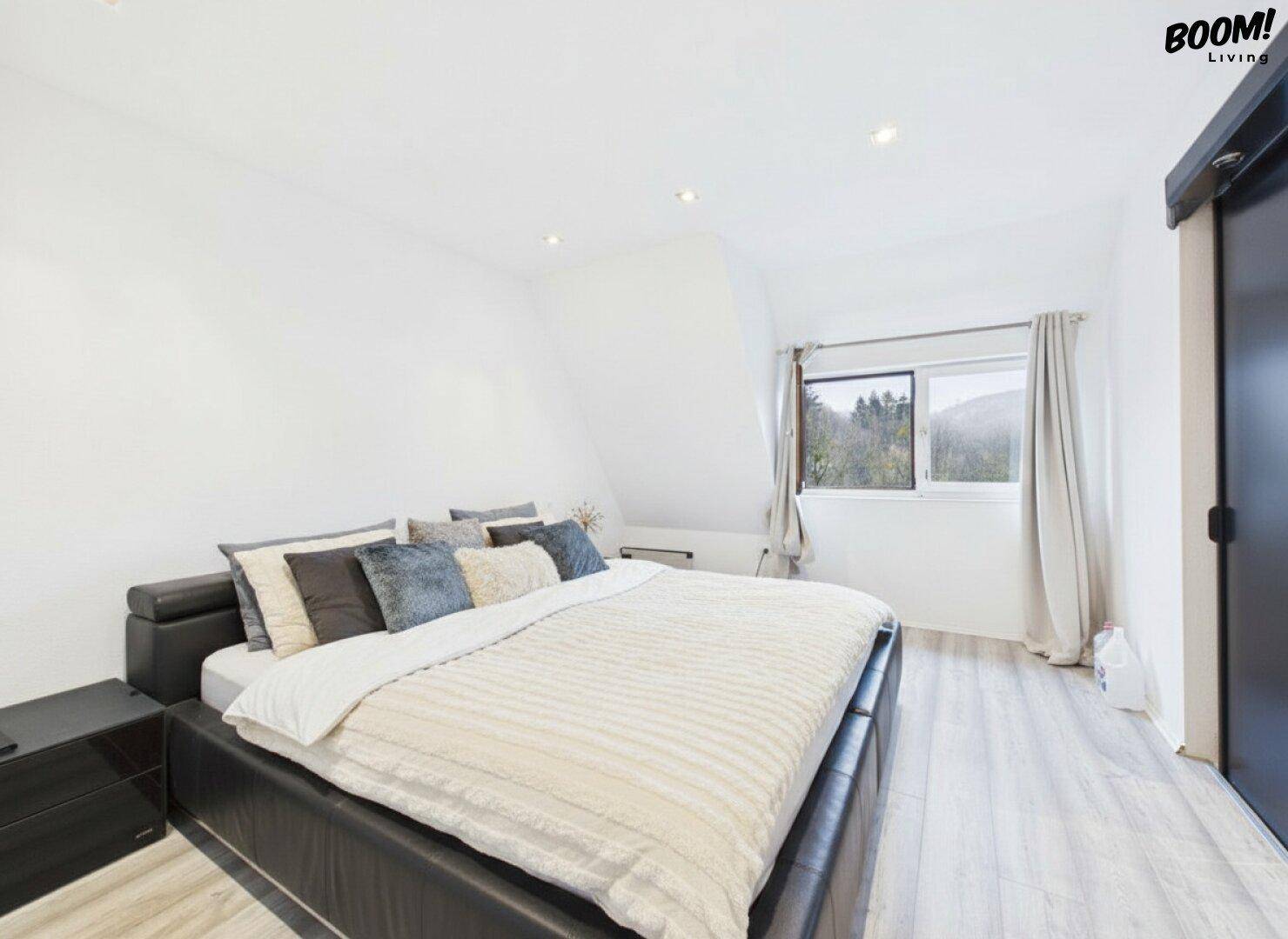 Gemütliches Schlafzimmer mit hellem Laminatboden, Doppelbett und Blick ins Grüne.