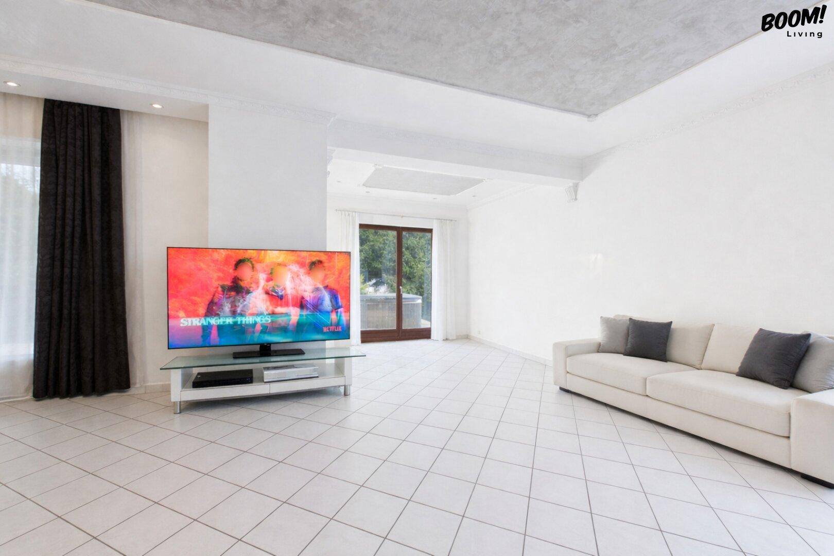 Helles Wohnzimmer mit Fliesenboden, großem Fernseher und bequemer Couch.