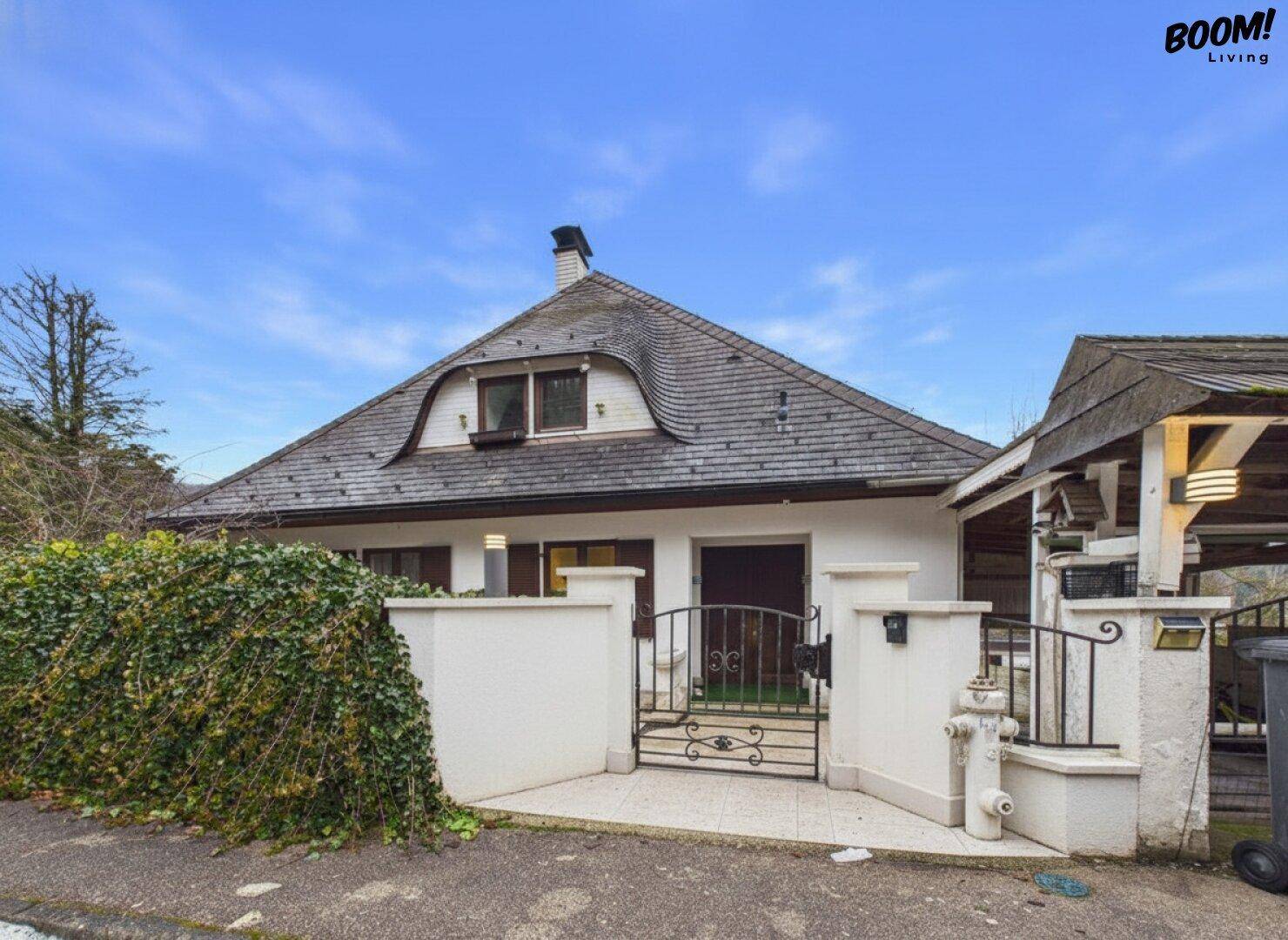 Vorderansicht des Hauses mit Mansarddach, weißer Fassade und schmiedeeisernem Eingangstor.