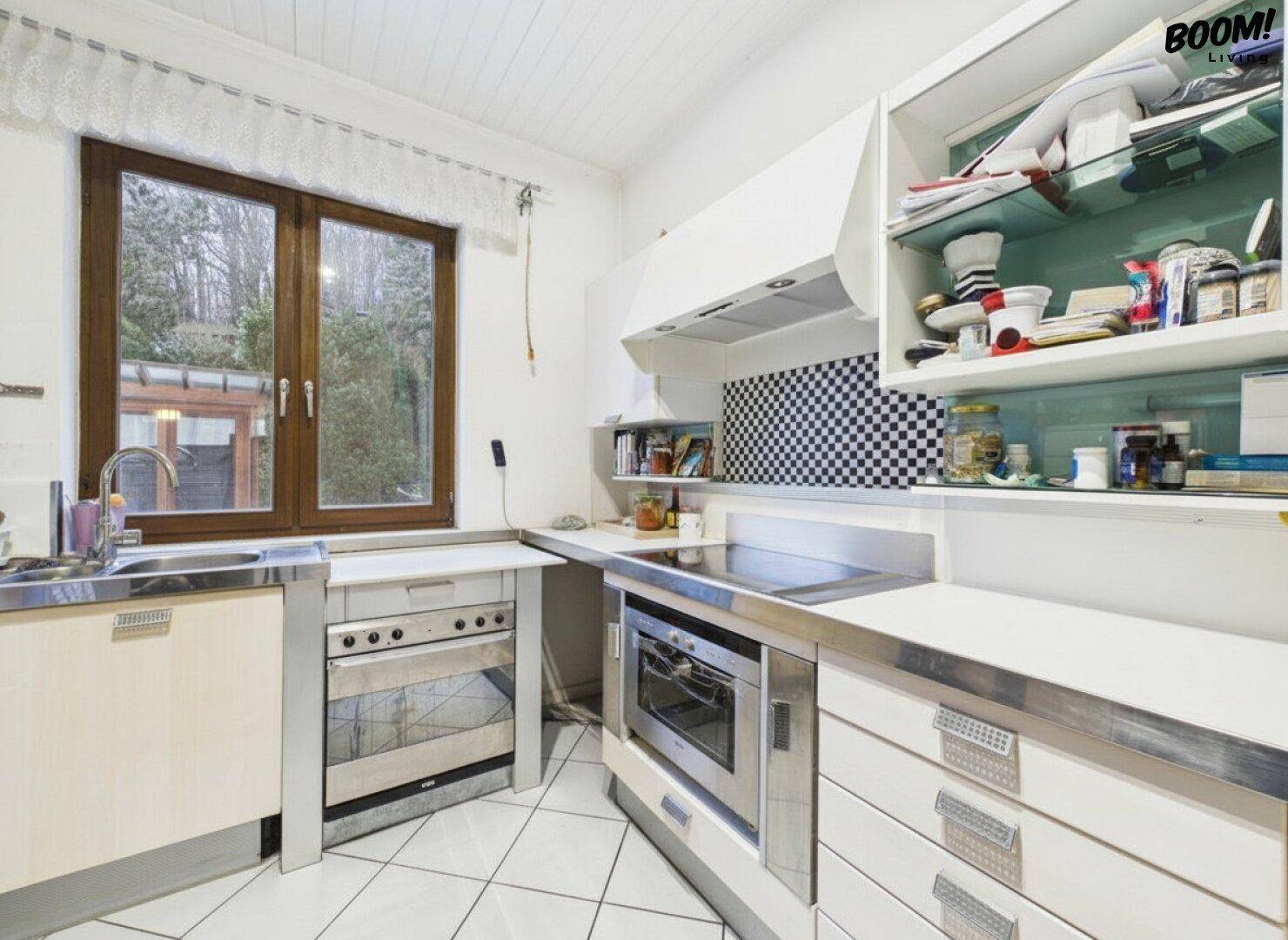 Funktionale Küche mit weißen Schränken, Edelstahloberflächen und Fenster mit Grünblick.