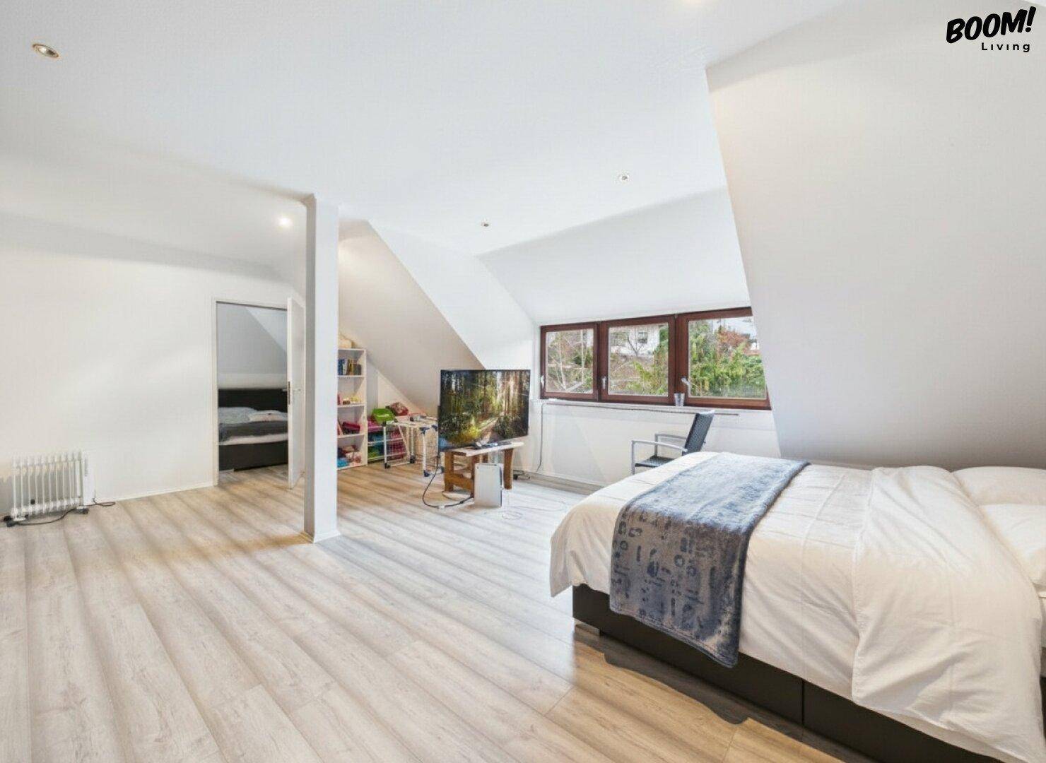 Geräumiges Schlafzimmer im Dachgeschoss mit schrägen Wänden und hellem Laminatboden.