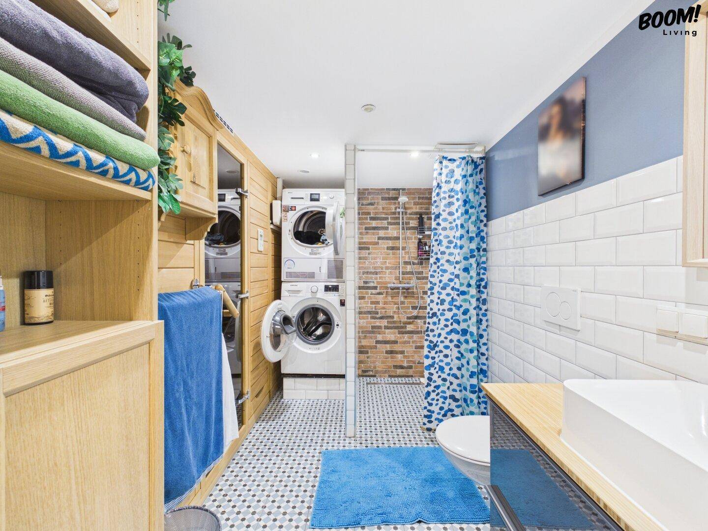 Badezimmer mit Dusche, Waschmaschine und Trockner, sowie praktischen Holzregalen.