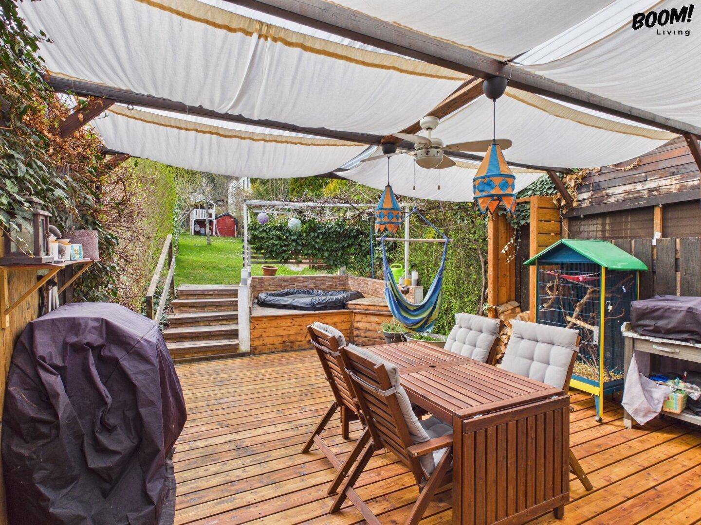 Überdachte Holzterrasse mit Esstisch, Hängematte und Blick in den Garten.