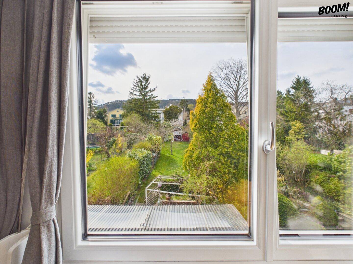 Fensterblick auf den grünen Garten und die umliegende Wohngegend mit viel Natur.