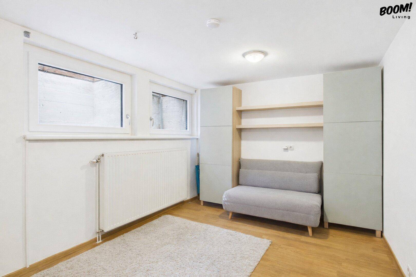 Heller Raum im Untergeschoss mit Sofa, Schränken und Fenstern zum Lichtschacht.