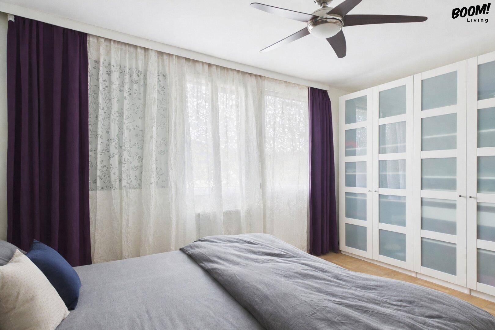Schlafzimmer mit großem Fenster, Einbauschränken und Deckenventilator für angenehmes Klima.