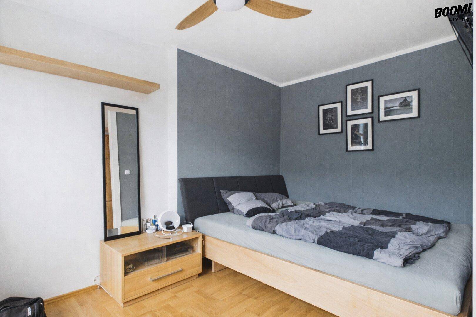 Schlafzimmer mit Holzboden, modernem Bett und grauer Akzentwand für eine ruhige Atmosphäre.