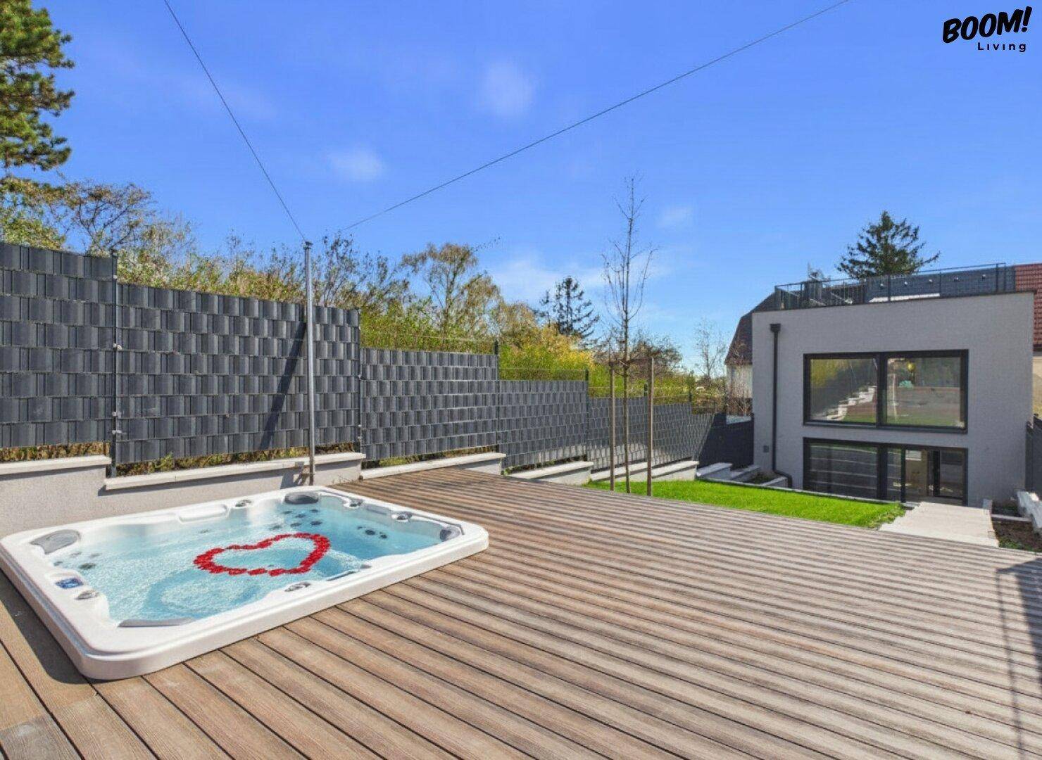 Große Holzterrasse mit integriertem Whirlpool und Blick auf das moderne Gebäude.