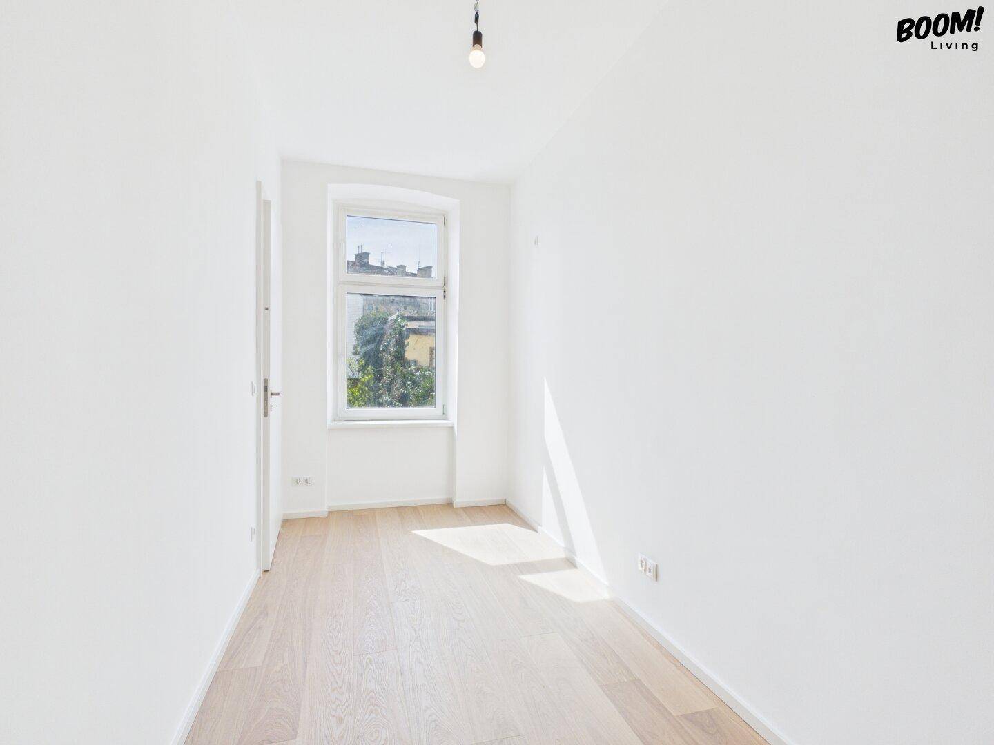 Leeres, helles Zimmer mit Holzboden und einem Fenster, ideal als Schlaf- oder Arbeitszimmer.