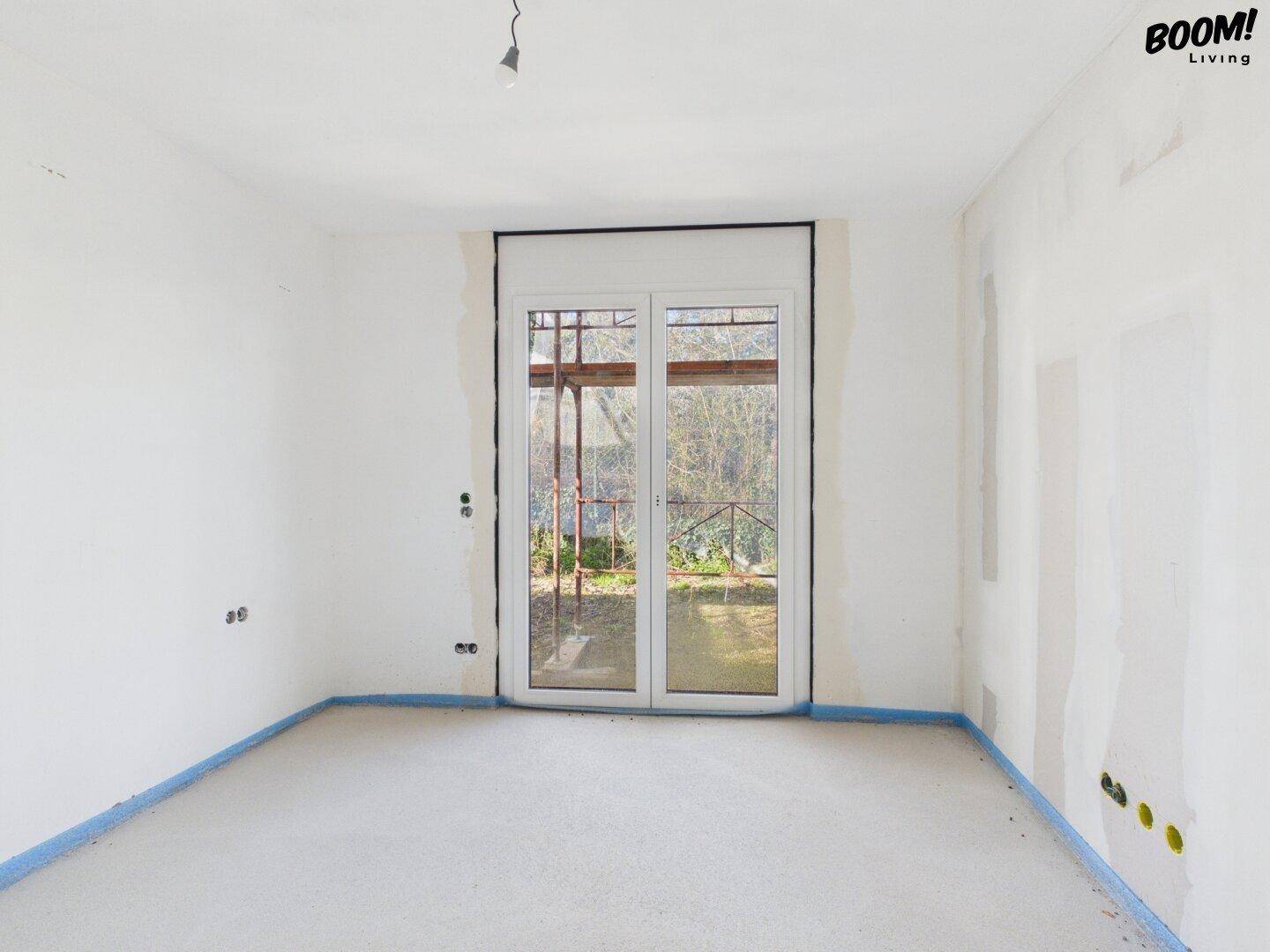 Unfertiger Raum im Rohbauzustand mit Fenster und Blick ins Freie.