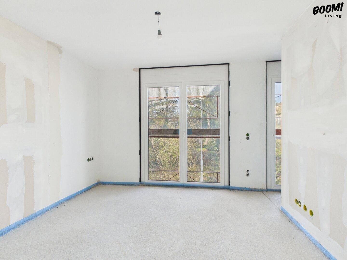 Rohbau eines Zimmers mit großer Fensterfront, die auf die Umgebung blickt.