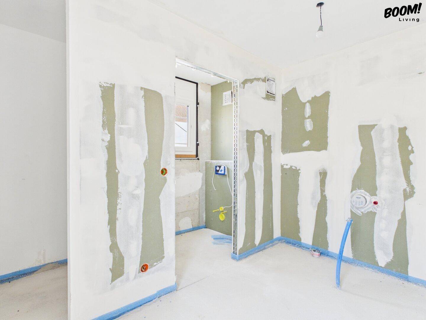 Rohbau eines Badezimmers mit sichtbaren Wasseranschlüssen und einem Fenster für Tageslicht.