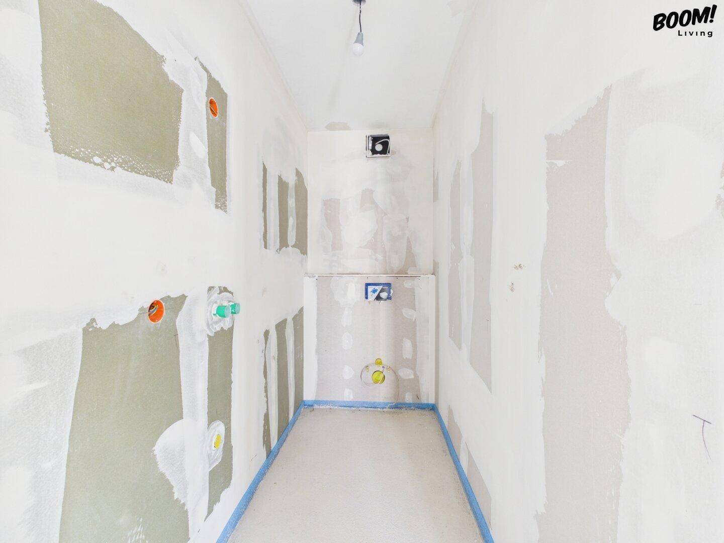 Unfertiges Badezimmer mit vorbereiteten Anschlüssen für Toilette und Waschbecken.