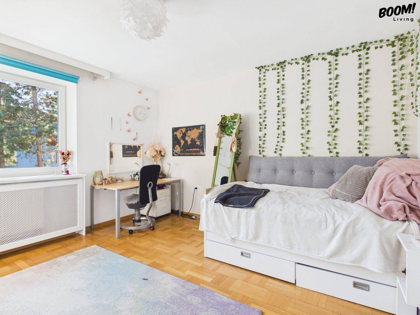 Jugendliches Schlafzimmer mit Holzboden, Tagesbett und Schreibtisch am Fenster.