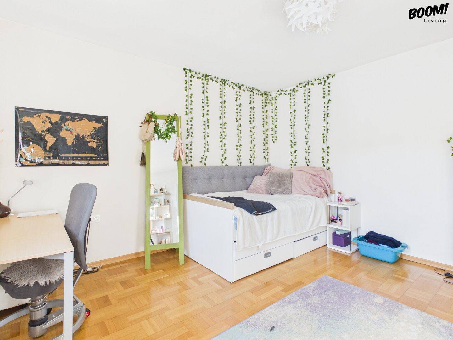 Helles Schlafzimmer mit Holzboden, Tagesbett und dekorativen Pflanzenranken an der Wand.