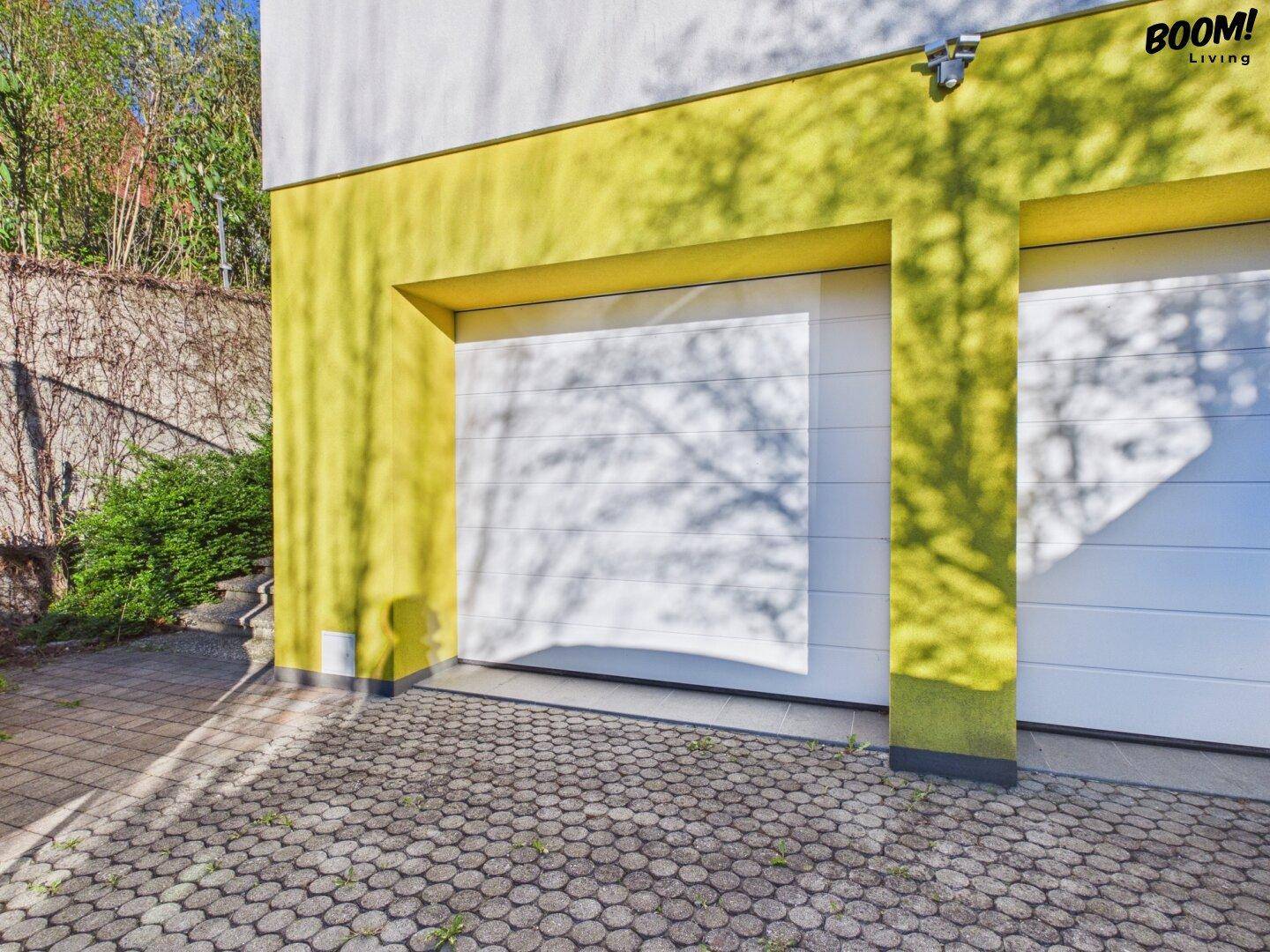 Moderne Garageneinfahrt mit gelber Fassade und gepflastertem Vorplatz.