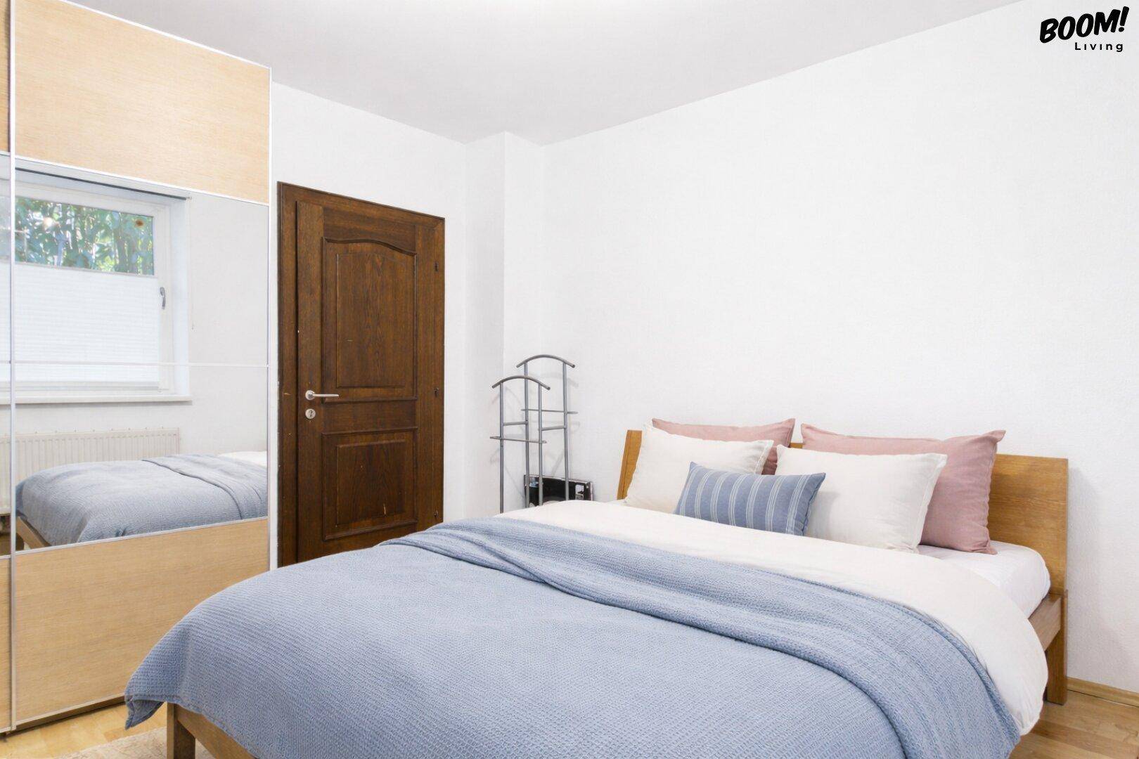 Schlafzimmer mit Doppelbett, hellem Holzboden und Spiegelschrank.