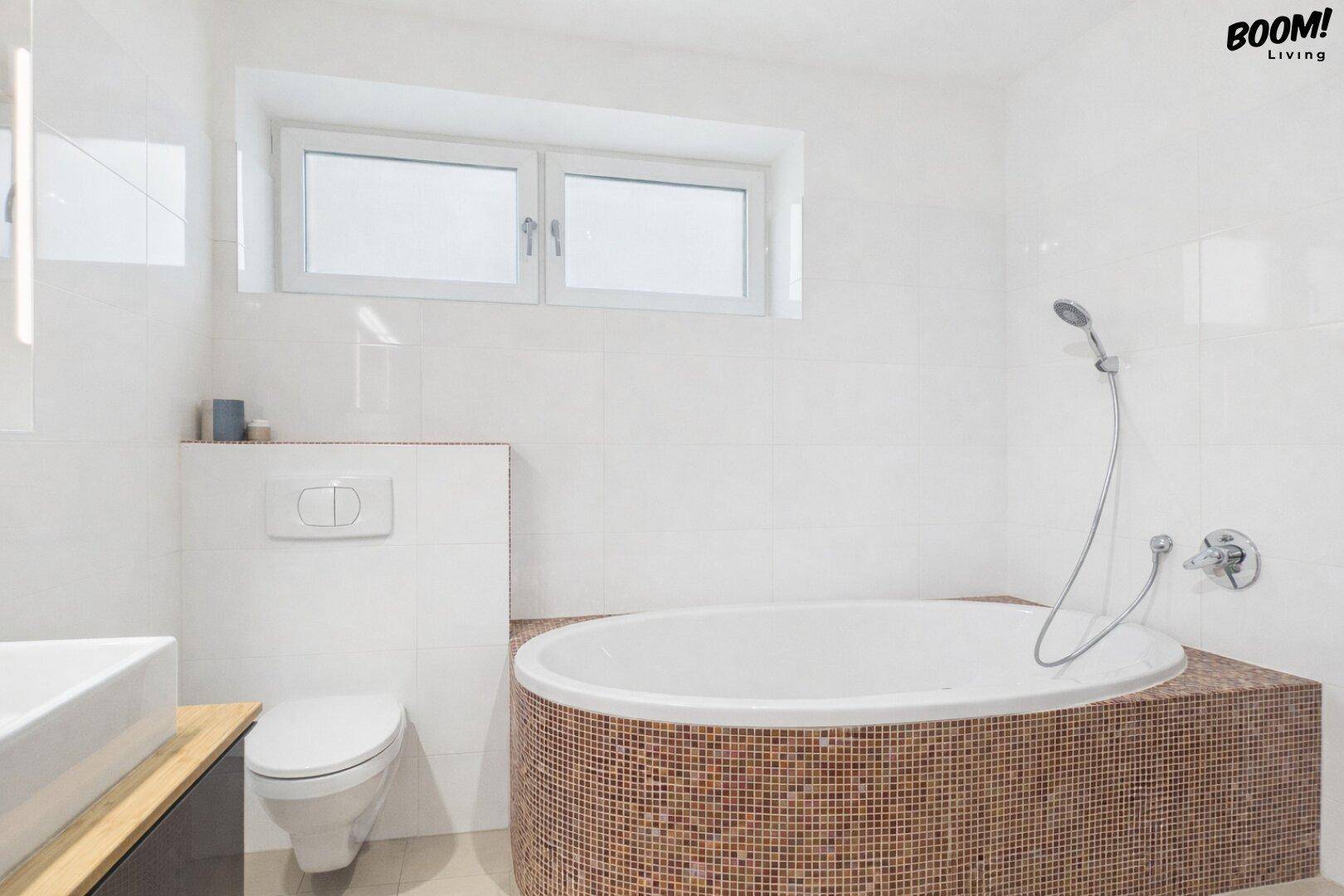 Modernes Badezimmer mit ovaler Badewanne, Wand-WC und Fenster für Tageslicht.