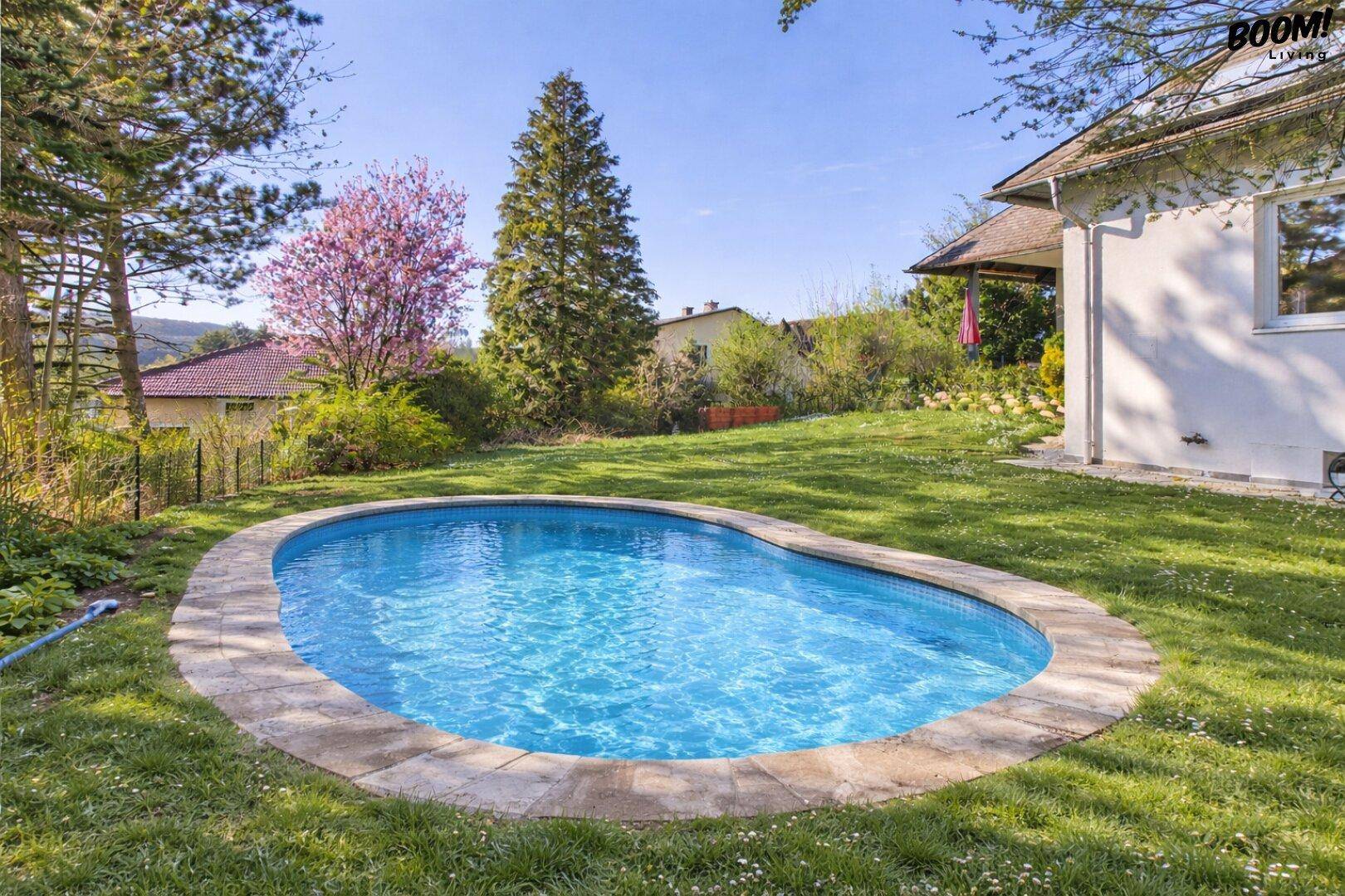Ovaler Swimmingpool im Garten mit gepflastertem Rand und umgebender Rasenfläche.