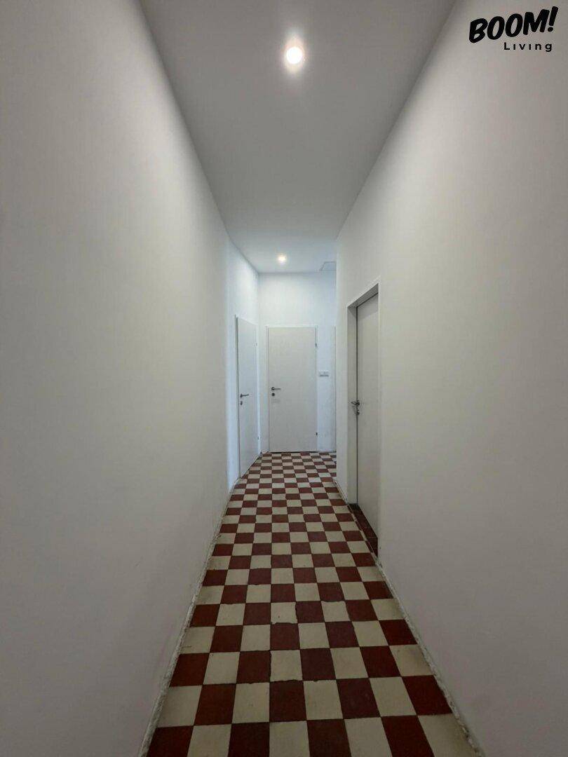 Langer Flur mit weiß gestrichenen Wänden und einem rot-weiß karierten Fliesenboden.