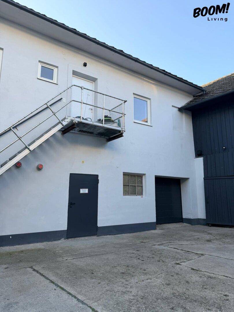 Rückseite eines Gebäudes mit Außentreppe und Garagentor in hellem Grau.