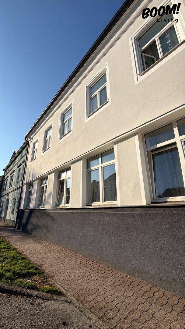 Seitenansicht eines Gebäudes mit vielen Fenstern und einem Gehweg davor unter blauem Himmel.