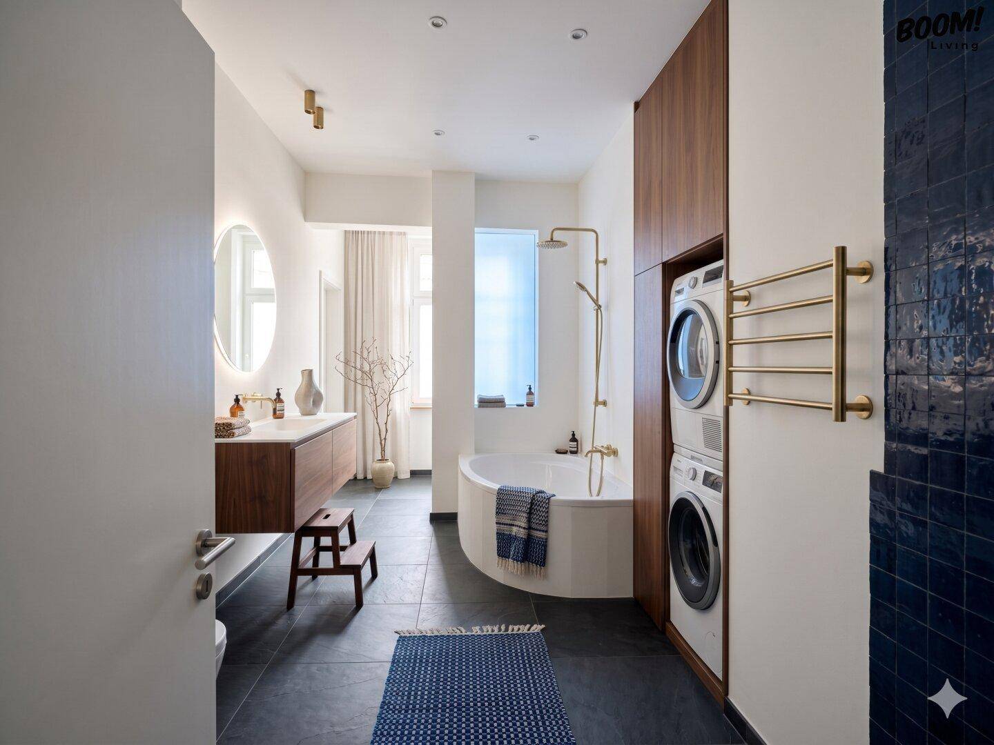 Modernes Badezimmer mit Badewanne, Dusche, Waschmaschine, Trockner und dunklen Fliesen am Boden.