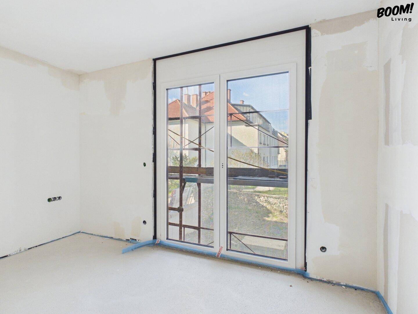 Rohbau eines Zimmers mit Fenstertür und Blick auf die umliegenden Gebäude.