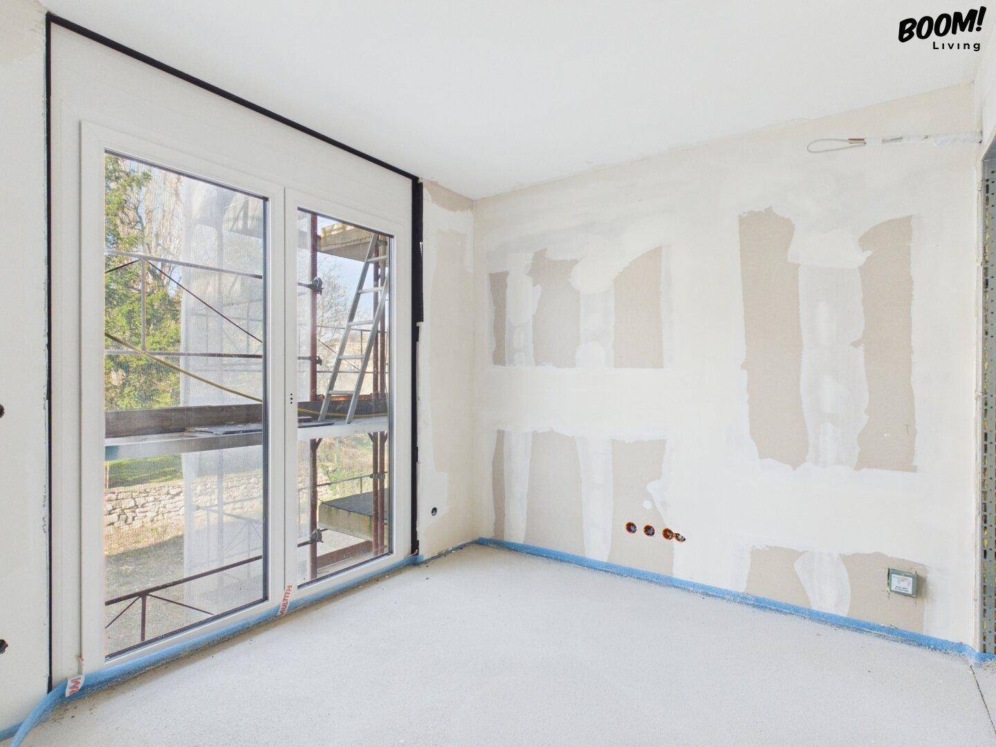 Rohbau eines Zimmers mit Fenstertür und Blick auf die Baustelle und Bäume.