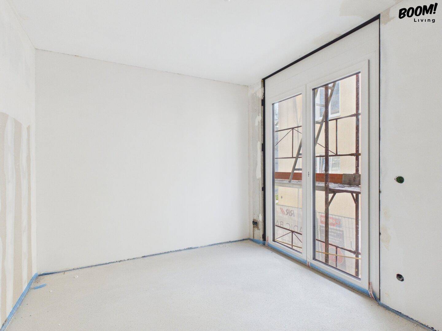 Rohbau eines Zimmers mit Fenstertür und Blick auf die umliegende Bebauung.