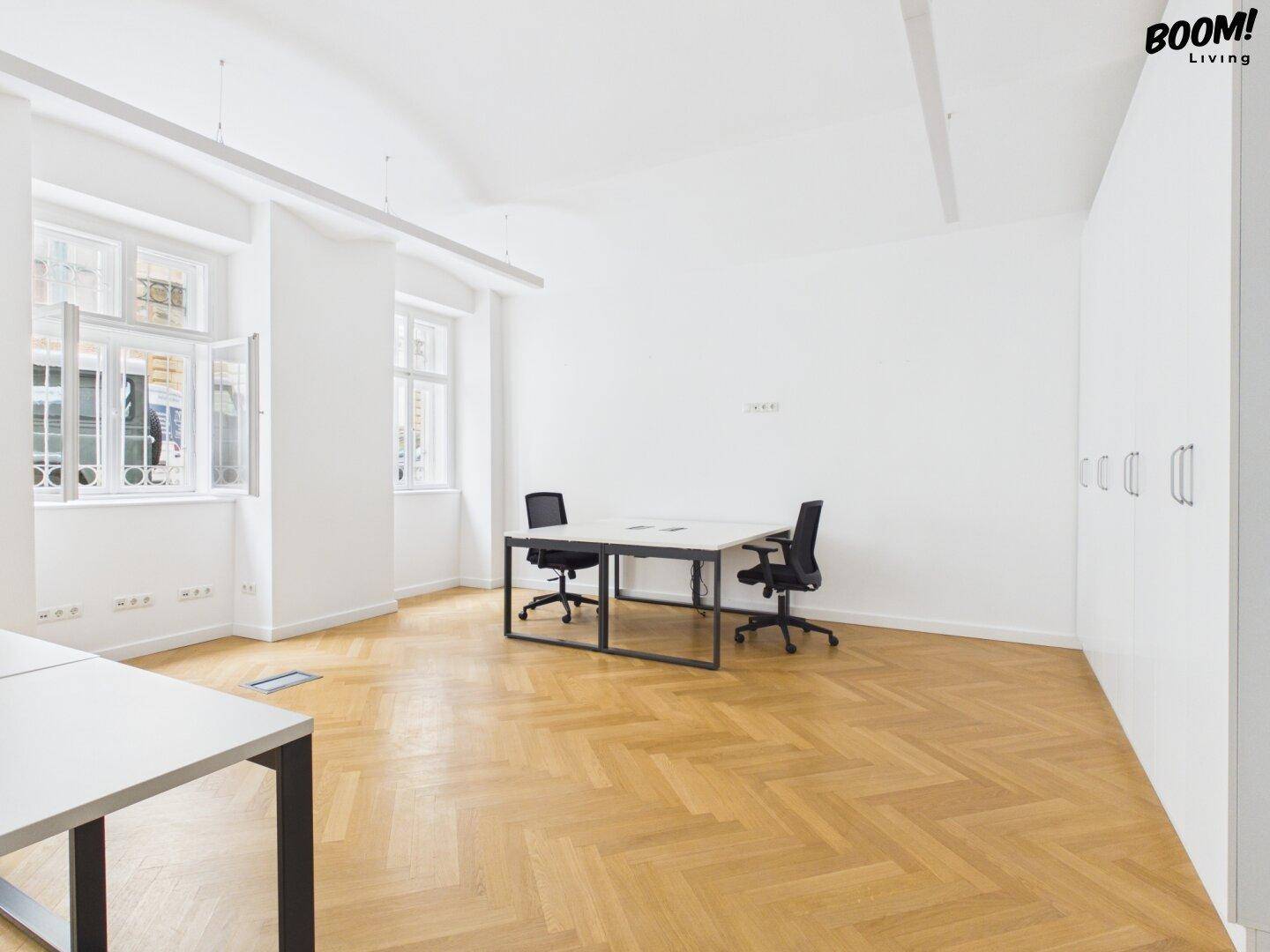 Geräumiges Büro mit Fischgrätparkett, hohen Decken und großen Fenstern mit Blick nach draußen.