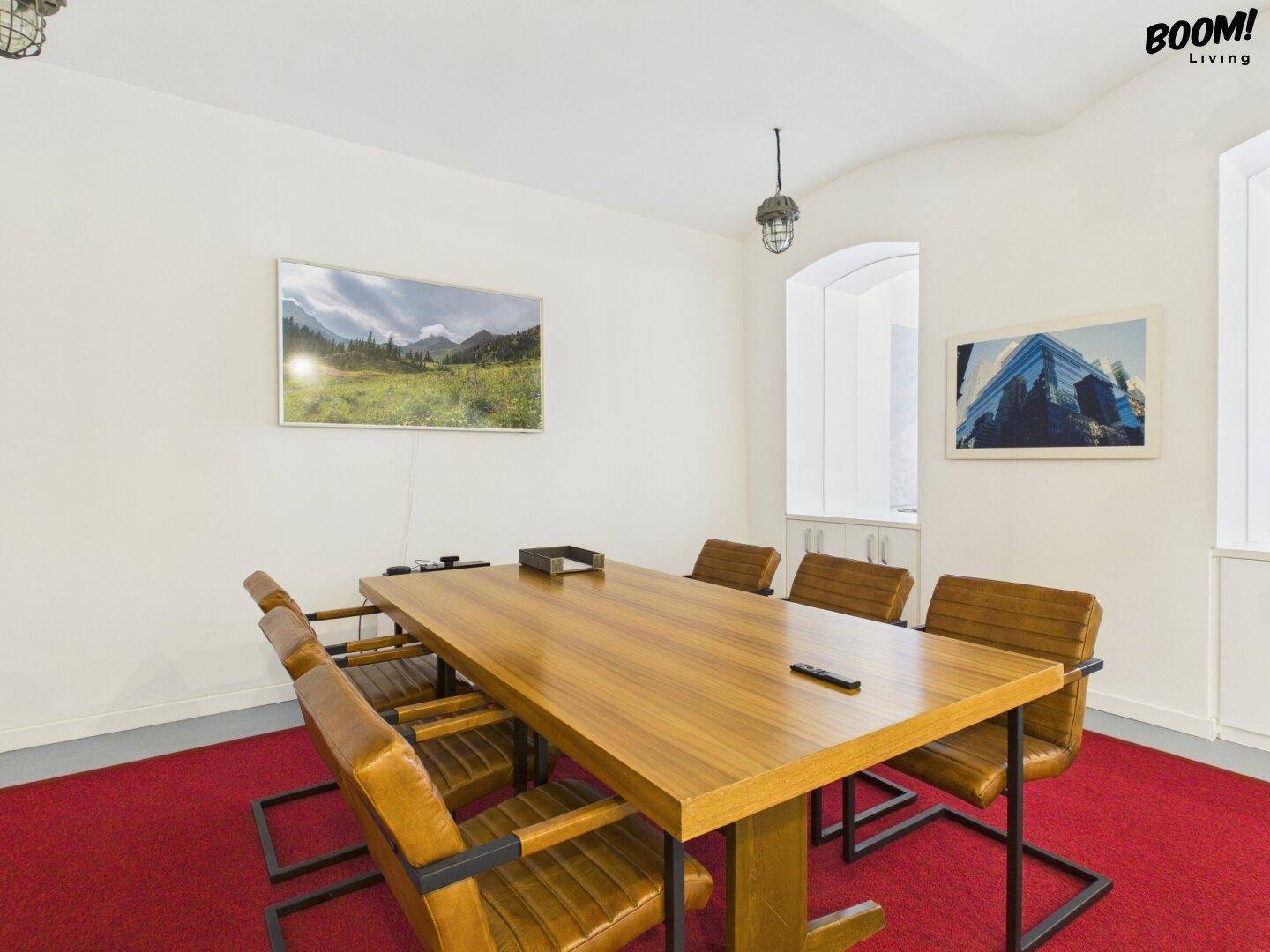 Konferenzraum mit großem Holztisch, bequemen Ledersesseln und einem an der Wand montierten Bildschirm.