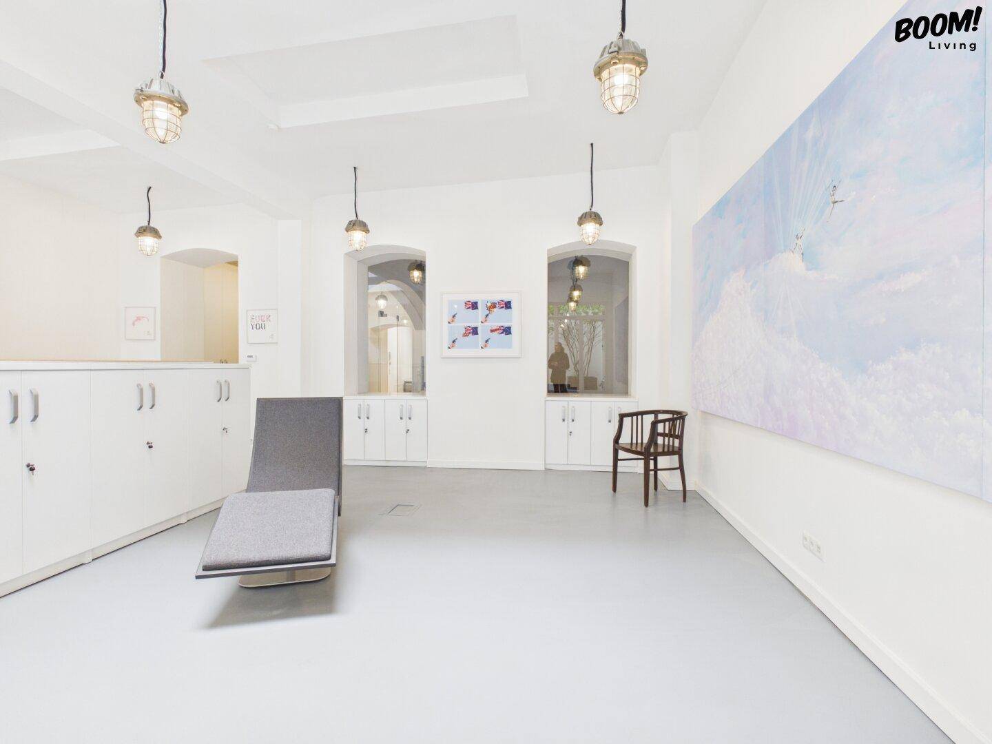Heller Büroraum mit moderner Liege, Einbauschränken und Kunst an den Wänden.